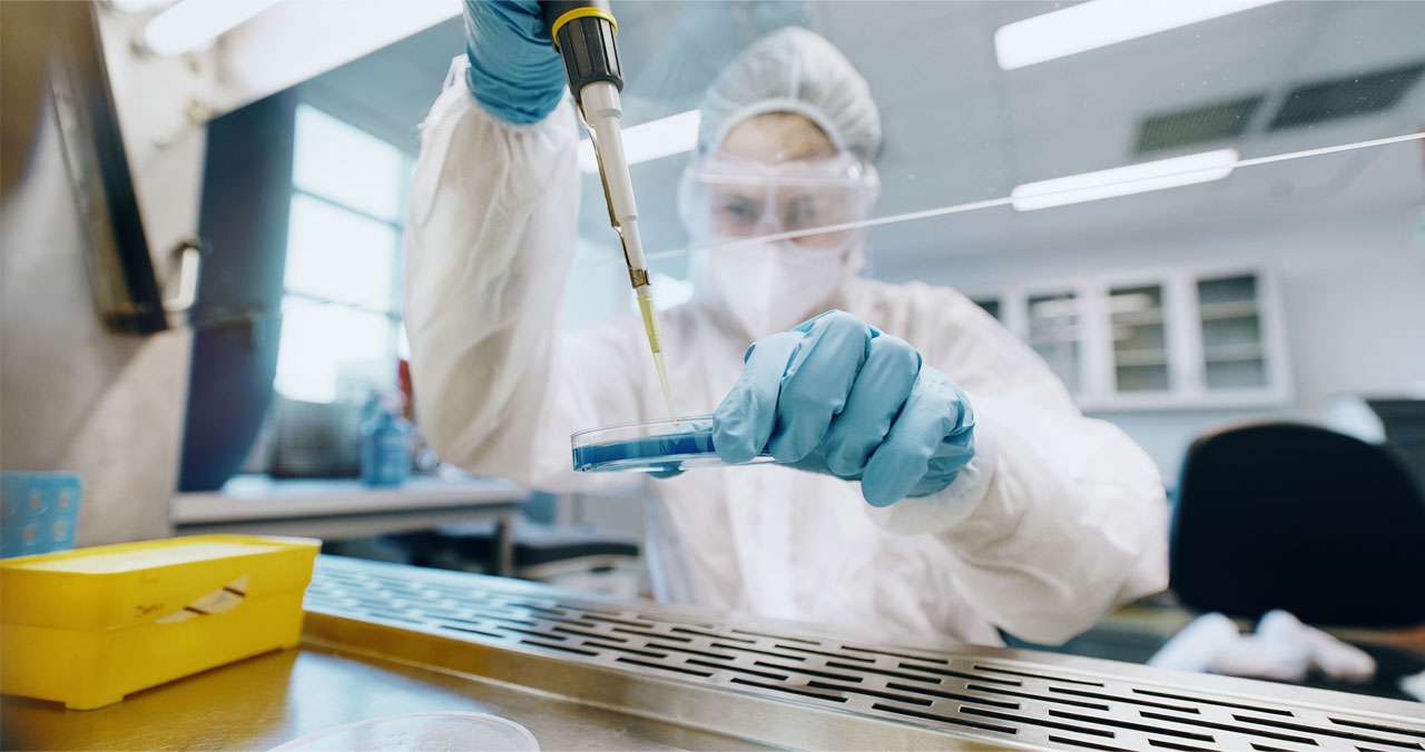 Fully PPE-covered Pii scientist working on HPAPIs in a biosafety fume hood.