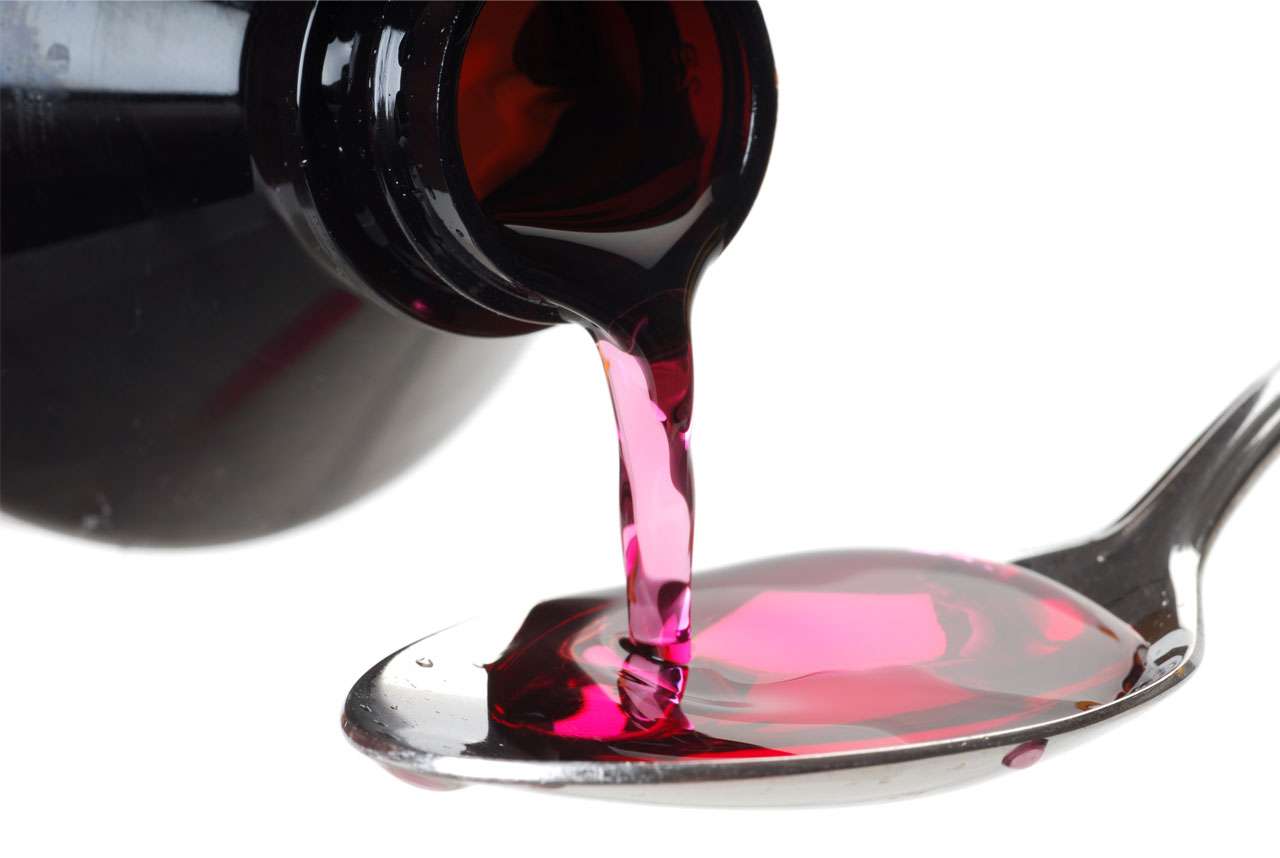 Pink oral liquid formulation being poured into a spoon.